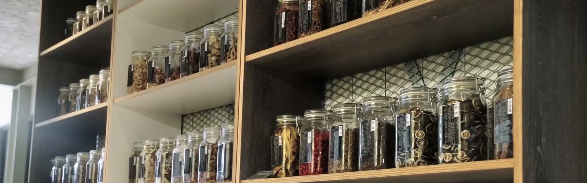 Glass jars of dried botanicals on wooden shelves